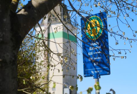 Bushaltestellenschild Husby Bahnhof vor Baum und blauem Himmel